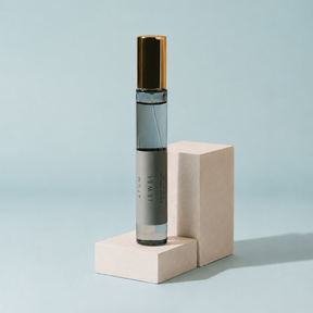A clear cylindrical perfume or fragrance roller bottle with a metallic gold cap and a gray label reading 'AFUN JEWEL', displayed upright on two light beige blocks against a pale blue background.