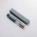 A slim cylindrical perfume bottle with a black cap and a gold-toned base, shown next to its rectangular gray box on a clean white background. The bottle and box are printed with the brand name 'ATUM OFFERINGS'.