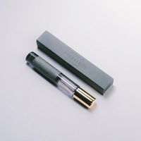 A slim cylindrical perfume bottle with a black cap and a gold-toned base, shown next to its rectangular gray box on a clean white background. The bottle and box are printed with the brand name 'ATUM OFFERINGS'.